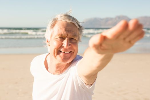 Happy senior man practicing yoga at beach on sunny day