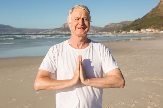 Portrait of smiling senior man doing yoga at beach on sunny day