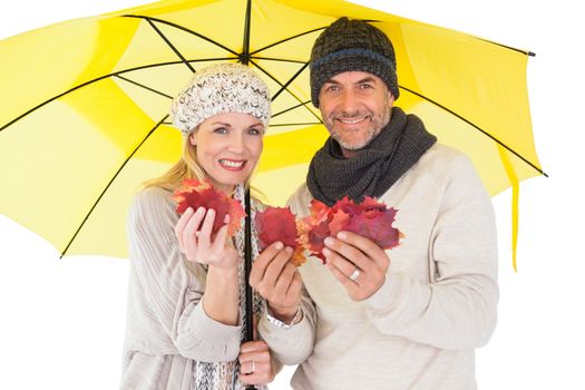 Couple in winter fashion showing autumn leaves under umbrella on white background