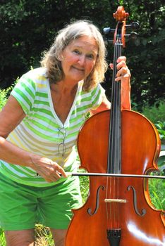 Mature female cellist with her instrument outside.