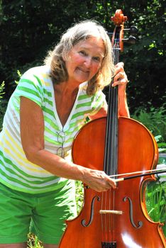 Mature female cellist with her instrument outside.