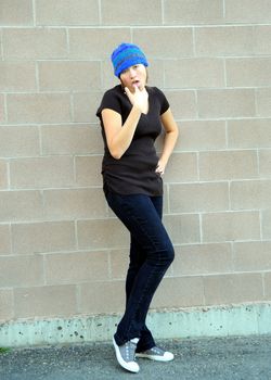 Female tomboy posing against a wall outside.