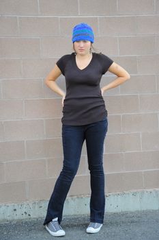 Female tomboy posing against a wall outside.