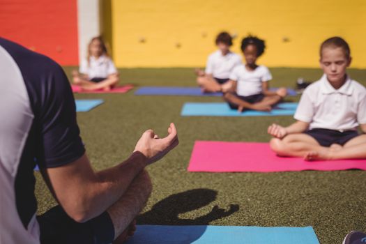 Coach and schoolkids practicing yoga in schoolyard