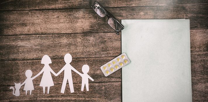 Overhead view of paper cut out family chain with medicine and file on table