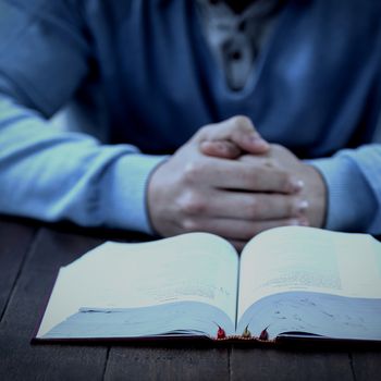 Mid section of man with bible praying at wooden table