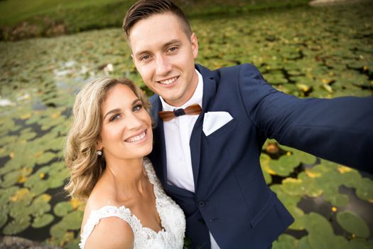 Wedding selfie. Bride and groom hugging, posing during photo shooting in park. Caucasian happy romantic young couple celebrating their marriage.