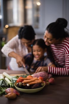 Vegetables on table against multi-generation family preparing food in kitchen at home