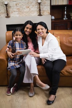 Portrait of smiling multi-generation family using digital tablet while sitting together on sofa at home