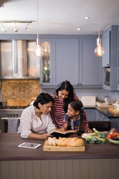 Multi-generation family reading book together in kitchen at home