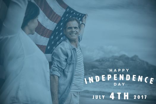 Happy 4th of july text on white background against mature couple holding american flag on beach
