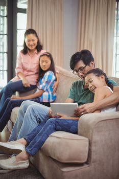 Smiling family using digital tablet together in living room at home