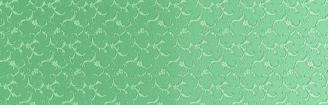 Embossed floral pattern on green paper. Textured paper with copy space. Light green, the color of fresh grass, paper surface, texture closeup.