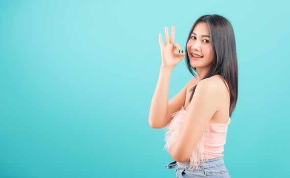 Portrait asian beautiful woman smiling showing finger OK sign and her looking to camera on blue background, with copy space for text