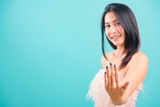 Smiling face Asian beautiful woman making gesture with hand inviting to come and her looking to camera on blue background, with copy space for text