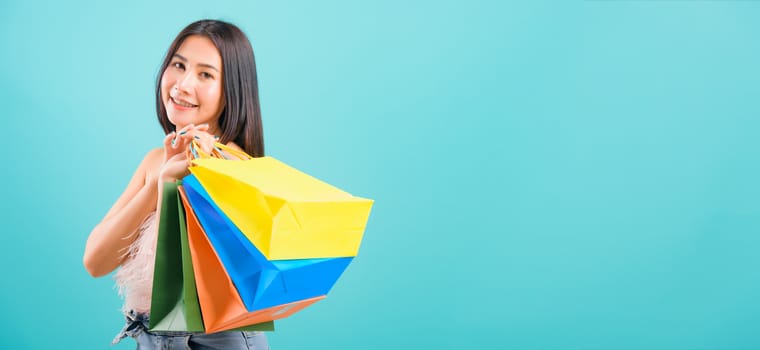 Portrait asian beautiful woman happy smiling her holding shopping bags multi color her looking to camera on blue background, with long copy space for text