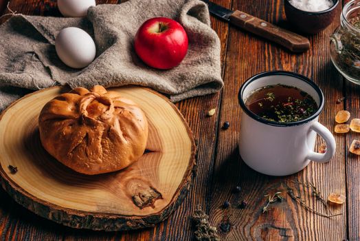 Rustic breakfast with traditional tatar pastry elesh, herbal tea in metal mug, apple and boiled eggs over dark wooden surface