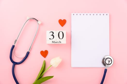 Doctor's Day concept, flat lay top view, equipment medical red heart stethoscope and note book on pink background, care patient in hospital with copy space for text