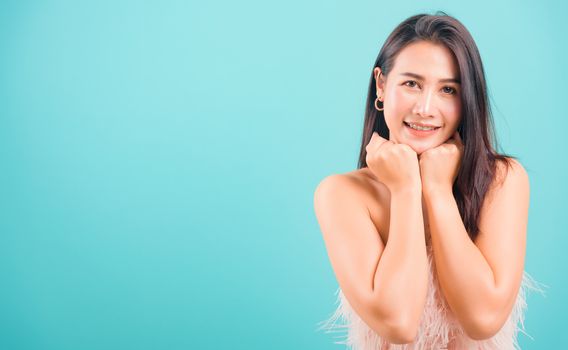Smiling face Asian beautiful woman her glad keeps both hands under chin smiles pleasantly on blue background, with copy space for text