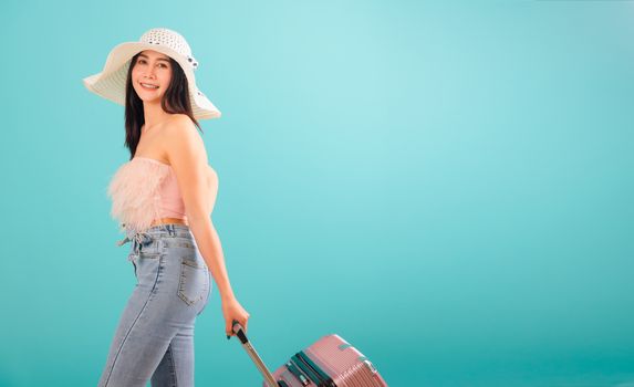 Portrait asian beautiful woman with hat her drag luggage or travel bag to travel weekends on blue background, with copy space for text