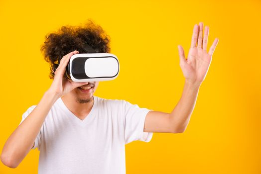 Asian handsome man with curly hair he using virtual reality headset or VR glass isolate on yellow background