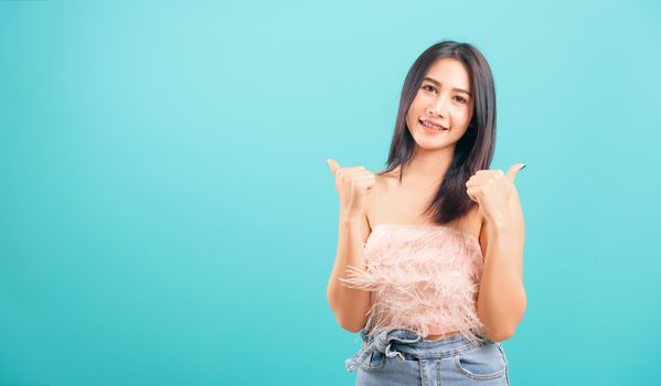 Portrait asian beautiful woman smiling showing hand showing thumbs up sign and her looking to camera on blue background, with copy space for text