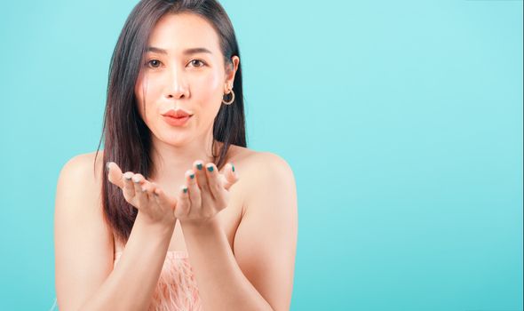 Smiling face Asian beautiful woman her blowing sending air kiss to hands on blue background, with copy space for text