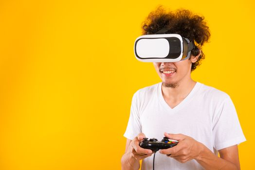 Asian handsome man with curly hair play game he using virtual reality headset or VR glass isolate on yellow background with copy space for text