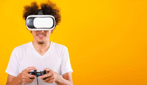 Asian handsome man with curly hair play game he using virtual reality headset or VR glass isolate on yellow background with copy space for text