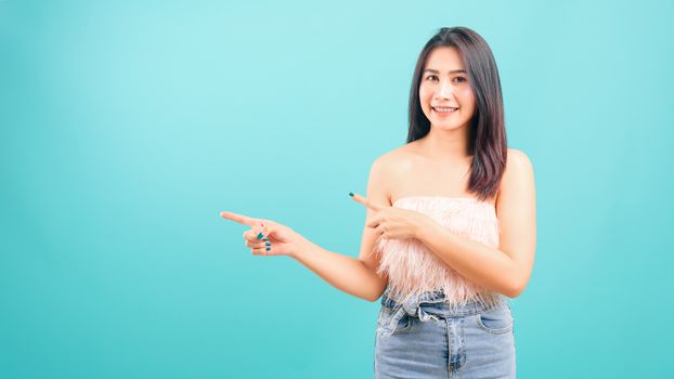 Portrait asian beautiful woman smiling looking camera her standing pointing finger out on blue background, with copy space for text