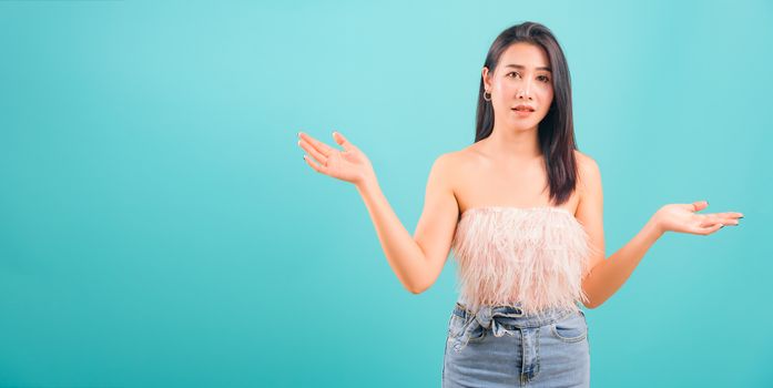 Asian beautiful woman her confused throwing hands aside on blue background, with copy space for text