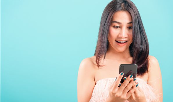 Smiling face portrait asian beautiful woman standing using mobile phone her excited on blue background, with copy space for text