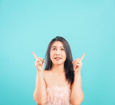 Smiling face Asian beautiful woman her point up on blue background, with copy space for text