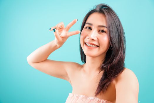 Smiling face Asian beautiful woman her selfie photo showing two finger on blue background, with copy space for text