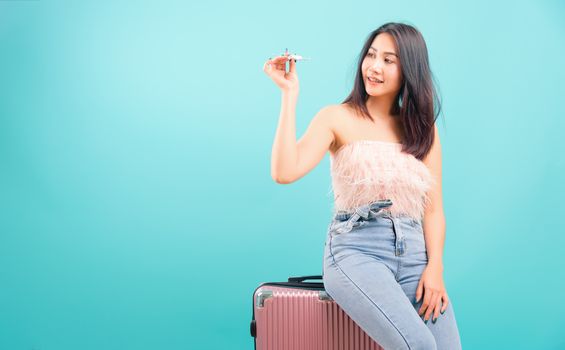 Portrait asian beautiful woman playing toy airplane model her sitting on luggage to travel bag on weekends on blue background, with copy space for text