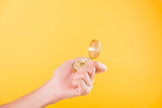 Hand holding antique brass compass isolated on yellow background with copy space for text