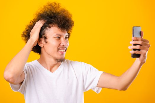 Portrait asian handsome man curly hair taking selfie with mobile phone isolated on yellow background