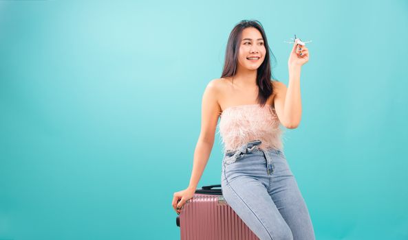 Portrait asian beautiful woman playing toy airplane model her sitting on luggage to travel bag on weekends on blue background, with copy space for text