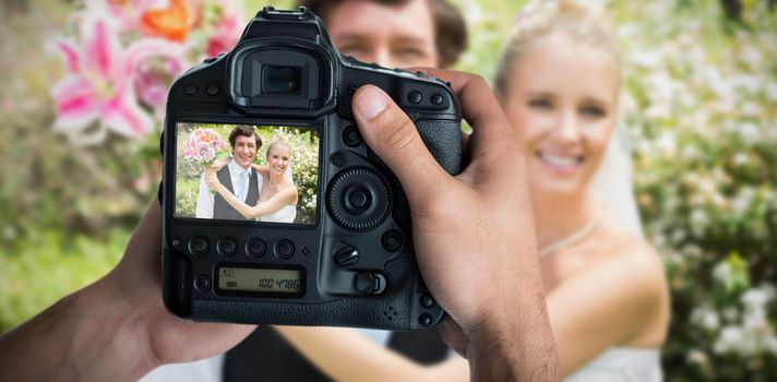 Cropped image of hands holding camera  against portrait of romantic newlywed couple 