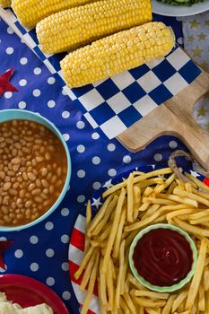 Close-up of french fries and corn cob on wooden table with 4th july theme