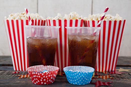 Popcorn, confectionery and drink on wooden table with 4th july theme