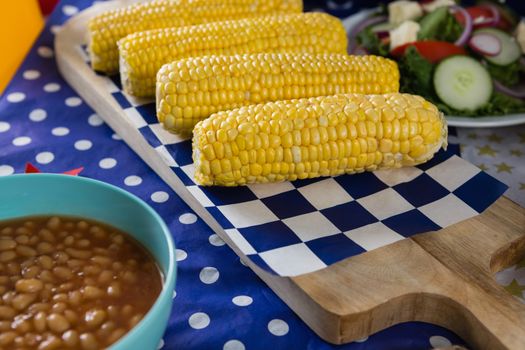 Close-up of baked beans and corn cob on wooden table with 4th july theme