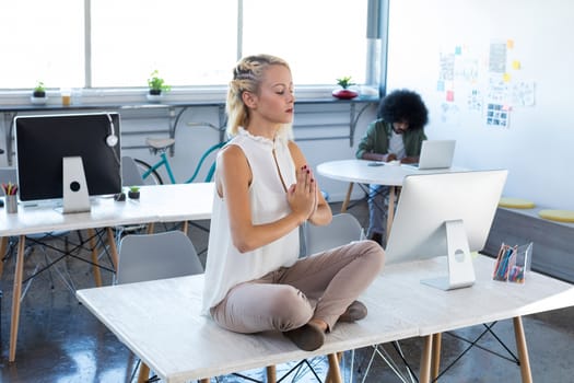 Female executives doing yoga on desk in office