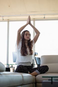 Young businesswoman with eyes closed doing yoga on sofa at office
