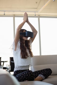 Young businesswoman mediating while using virtual reality on sofa in office