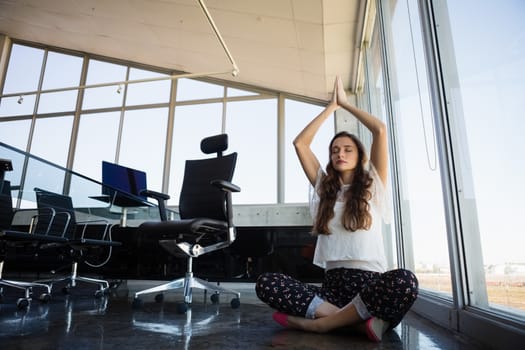 Young businesswoman with eyes closed doing yoga on floor at office