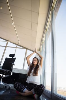 Full length of businesswoman with eyes closed doing yoga at office