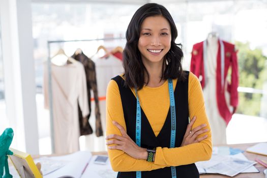 Portrait of smiling fashion designer standing with arms crossed in office