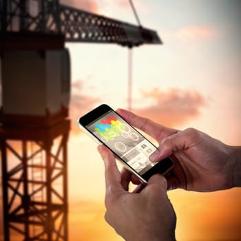 Close-up of man holding smart phone against 3d image of crane against sky