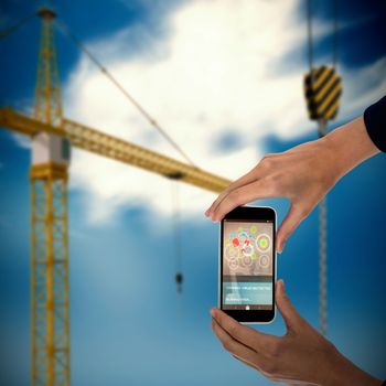 Cropped hands of businesswoman holding mobile phone against 3d image of yellow crane